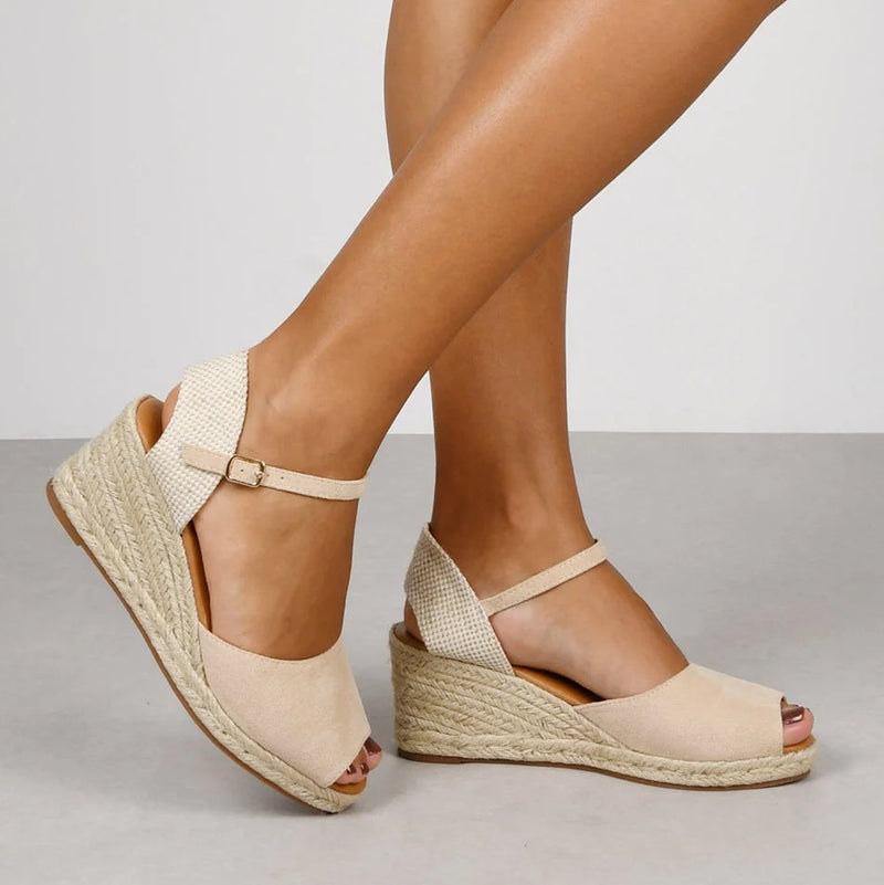 Sandalias beige con cuña de esparto y tira al tobillo con hebilla, puestas sobre un fondo gris claro