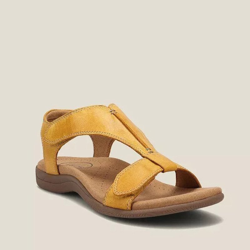 Sandalia plana amarilla con tiras de velcro y plantilla marrón con forma curva, sobre un fondo claro