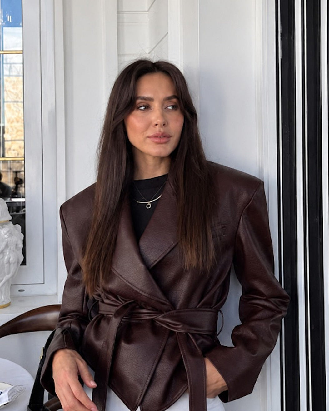 Chaqueta cruzada con cinturón en marrón oscuro, con camiseta negra y vaqueros blancos anchos