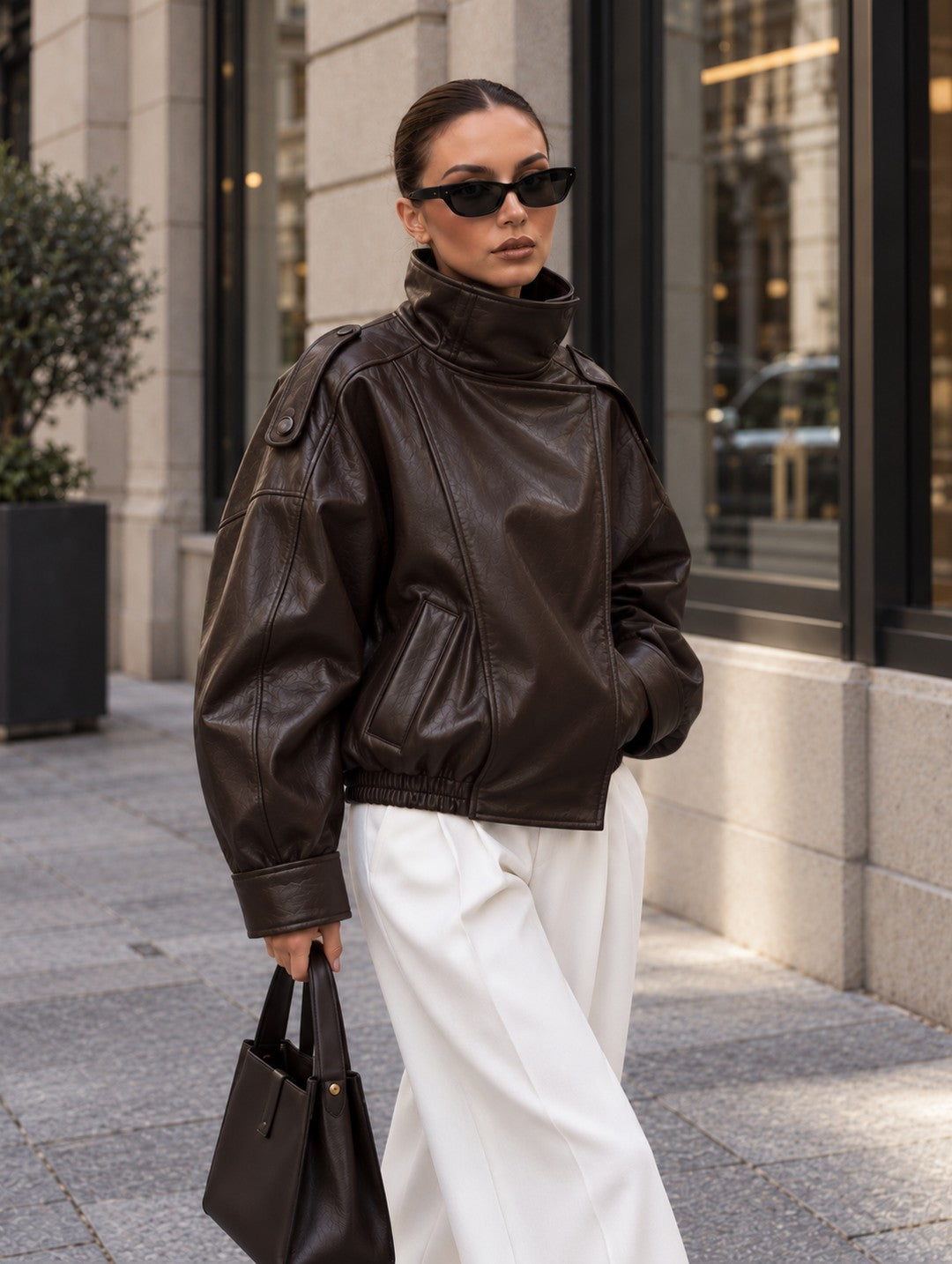 Cazadora efecto piel oversize marrón con cuello alto y bolsillos laterales, con pantalón blanco y bolso marrón