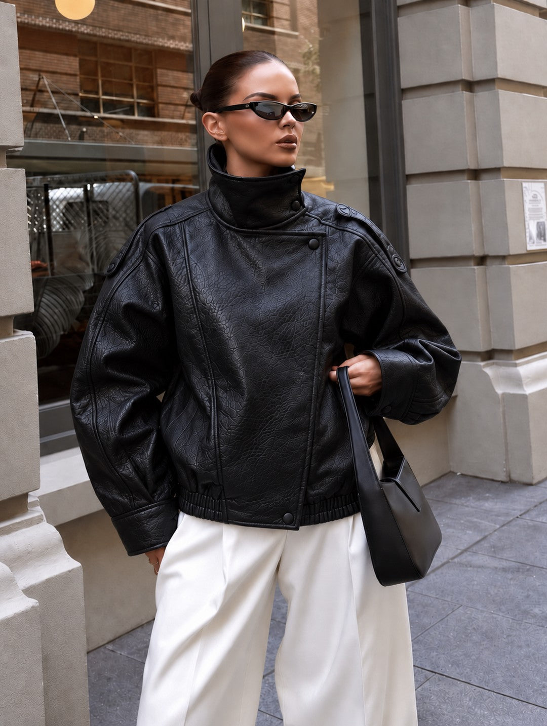 Cazadora efecto piel oversize negra con cuello alto, pantalón blanco y bolso negro